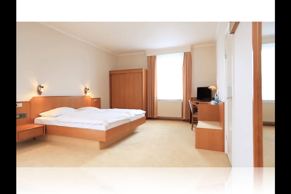 A modern hotel room with a large bed, bedside tables, a desk with a chair, and a television.