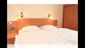 Une chambre d’hôtel avec une tête de lit en bois, deux oreillers blancs, une table de chevet avec un téléphone et des lampes fixées au mur.