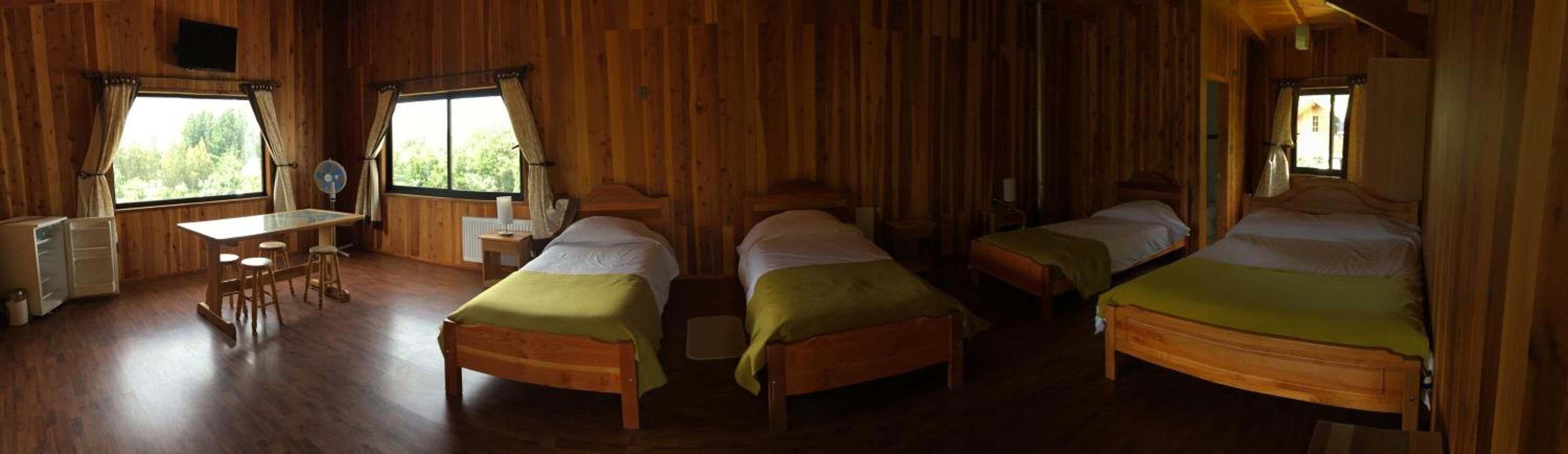 A wooden cabin with two single beds, a small table with stools, and a window with curtains.