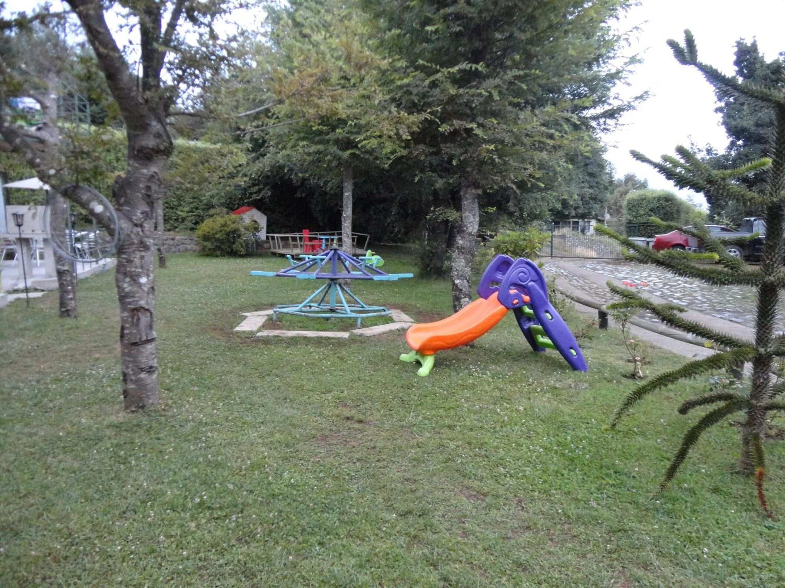 A playground with a slide and swings in a grassy area with trees.