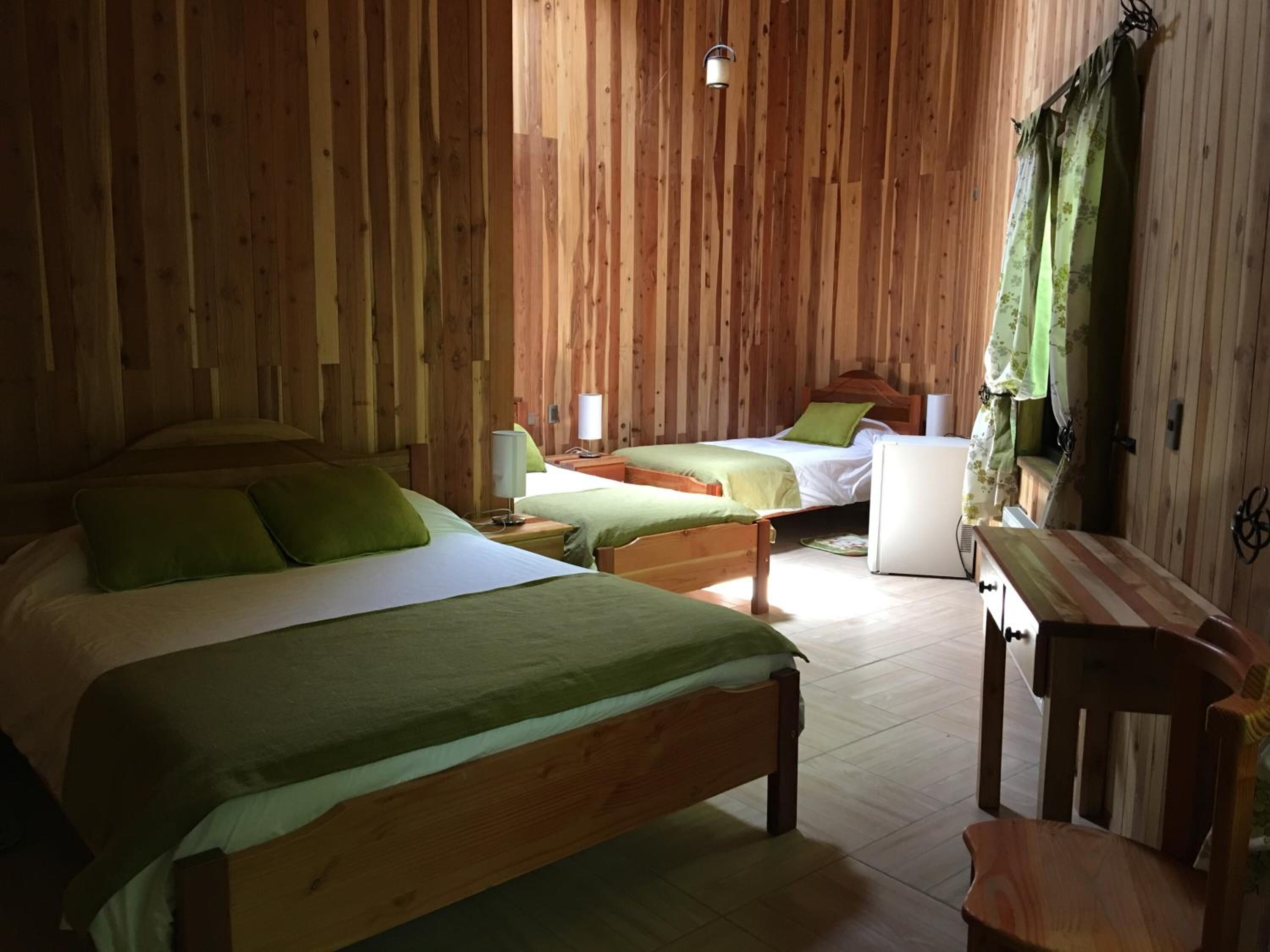 Una habitación con paneles de madera, dos camas, una mesita y una silla.