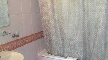 A bathroom with a white sink, a bathtub with a white towel, and a toilet with a sign.