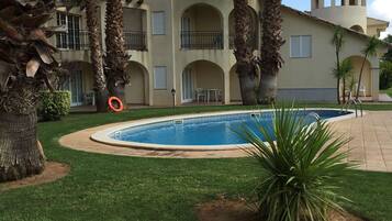 A pool surrounded by palm trees and a building with multiple balconies.