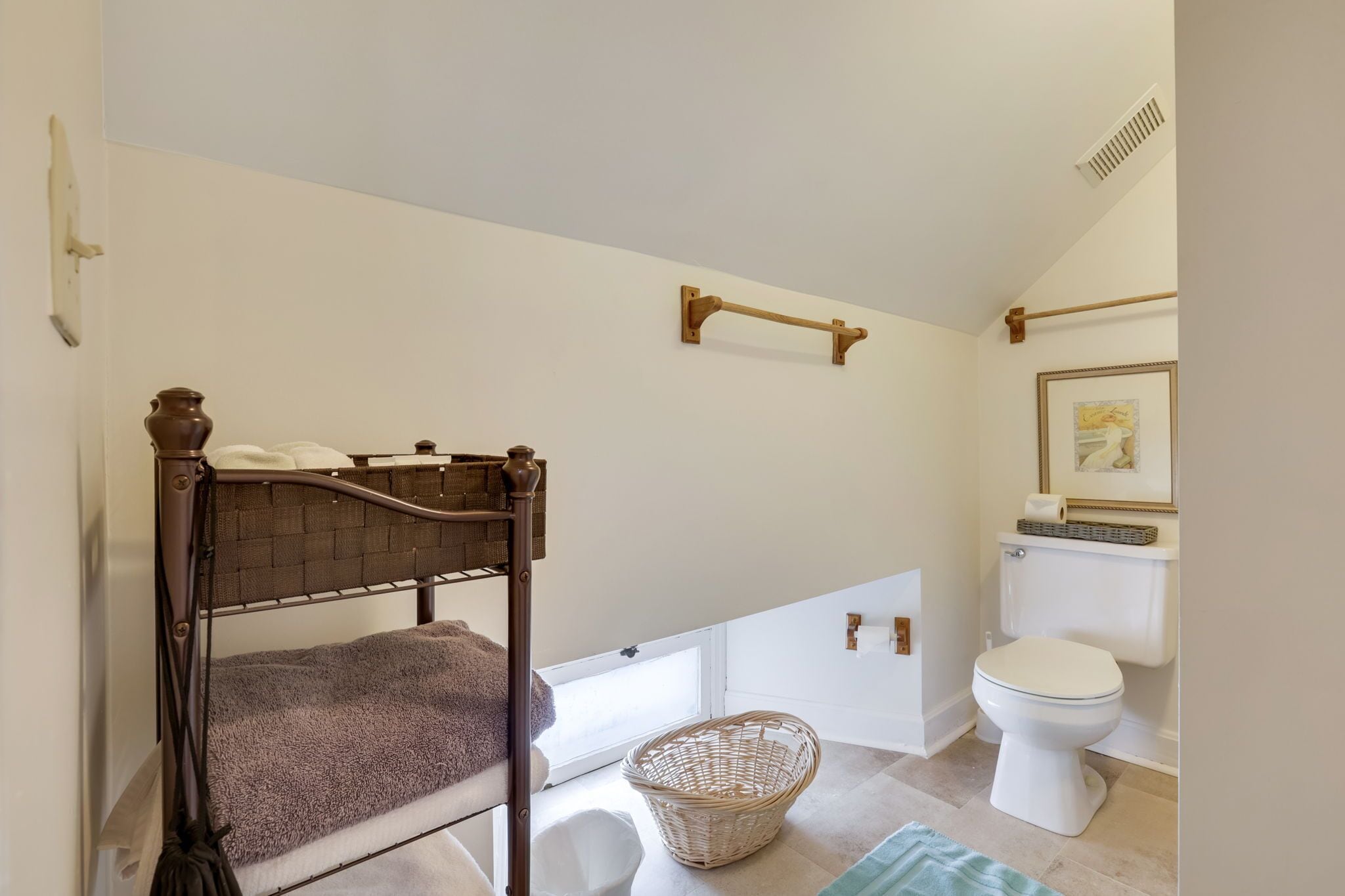 A bedroom with a wooden bed, a wicker basket, a white toilet, and a framed picture on the wall.