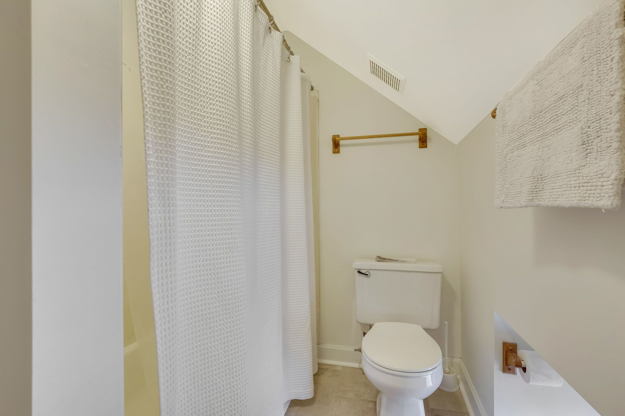Un baño pequeño y limpio con inodoro blanco, cortina de ducha y toallero.