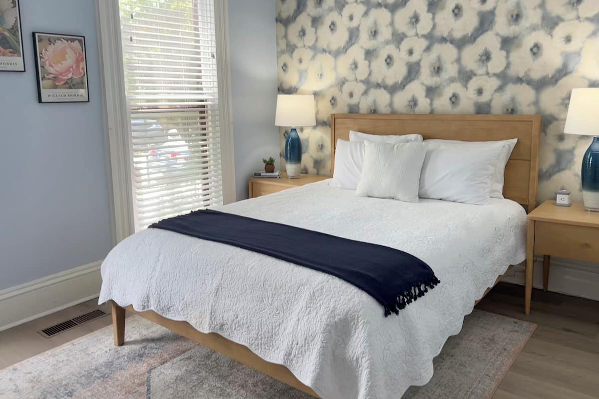 A neatly made bed with a white and navy blue blanket, a wooden headboard, and two bedside lamps.