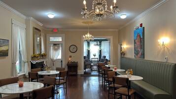 A hotel dining area with chandeliers, round tables, and a green booth.