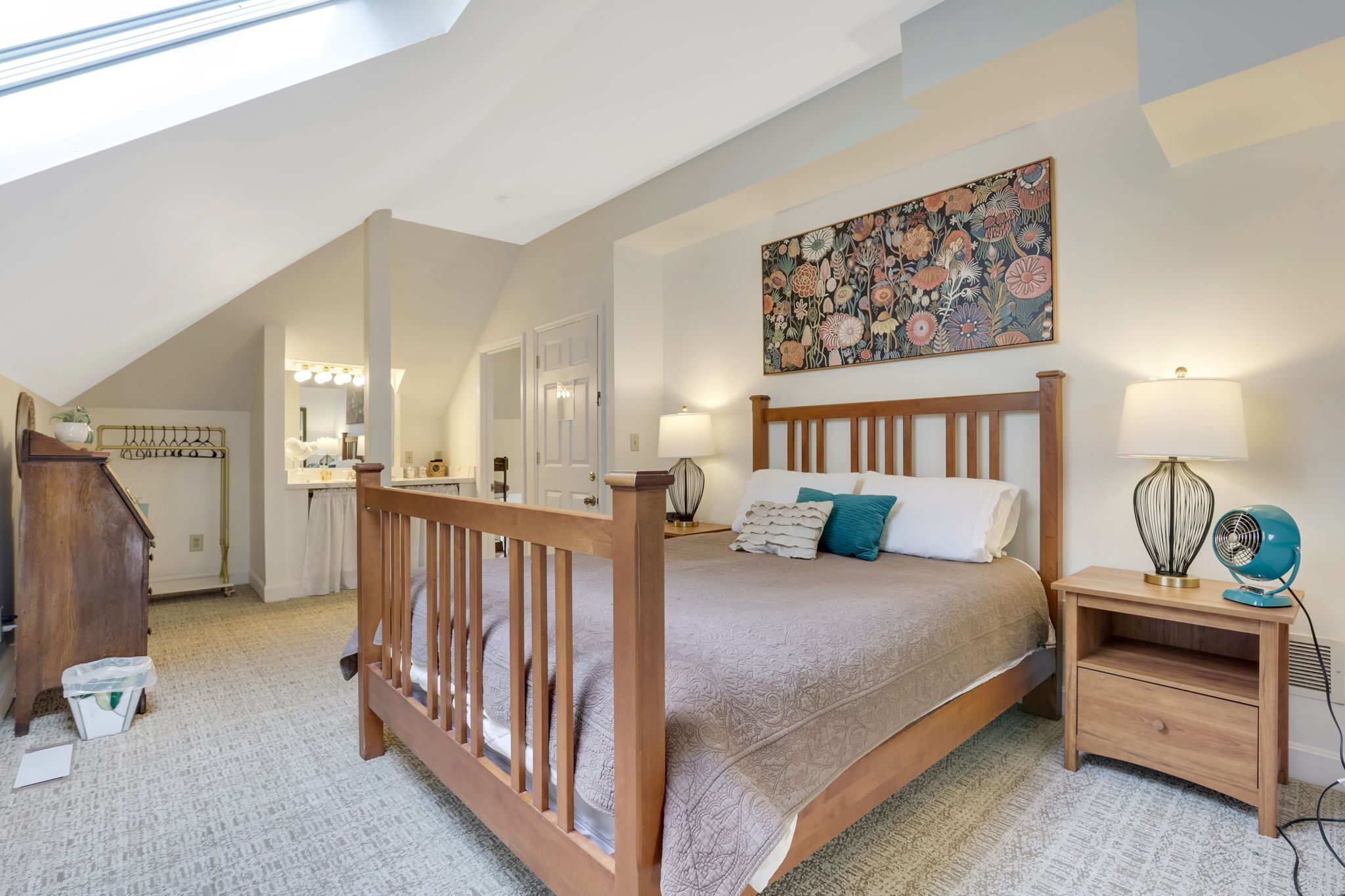 A bedroom with a wooden bed, bedside lamps, a nightstand, a wall-mounted artwork, and a skylight.