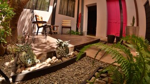 An outdoor patio with a wooden table and chairs, surrounded by decorative owl sculptures and a pebble pathway. - Hotel el Sole - Hostel (Santa Ana)