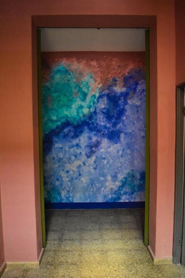 A hallway with a colorful abstract mural on the wall, a carpeted floor, and a door on the right.