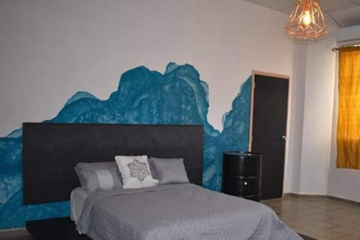 A bedroom with a bed, a headboard, a wall mural, a door, and a floor lamp.