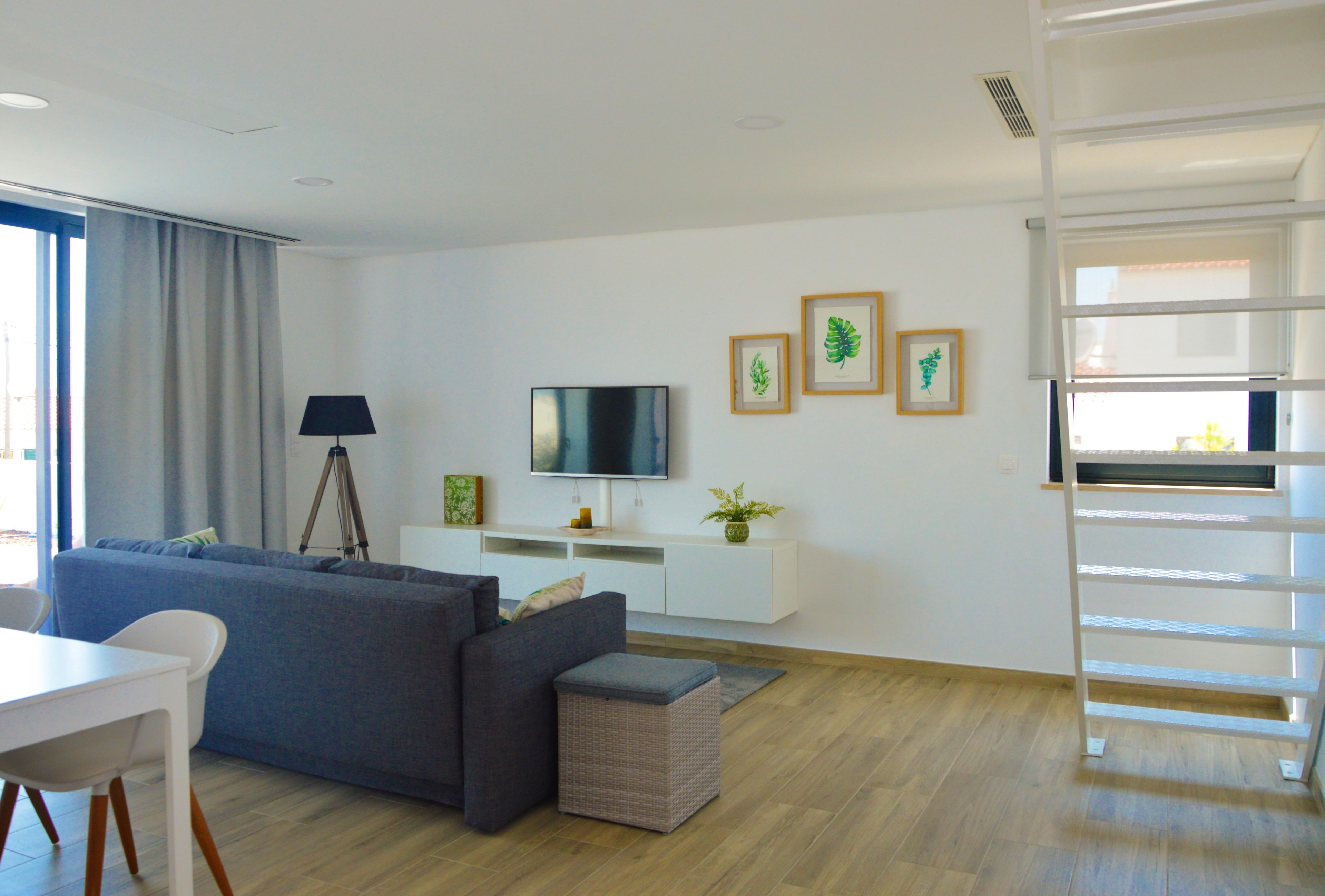 A modern living room with a grey sofa, a TV, framed artwork, and a white console.