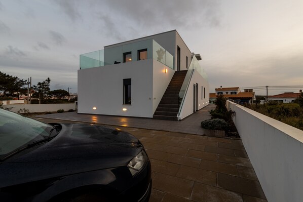 A modern house with a glass facade, a staircase leading to the upper level, and a car parked in the driveway.