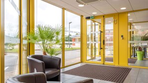 A hotel lobby with a yellow door, a reception desk, and a large window.