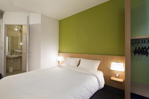 Hotelkamer met een bed, nachtkastje met lamp, groene accentmuur en een badkamer door een open deur zichtbaar.