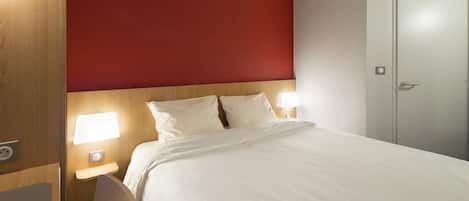 Habitación de hotel con una cama grande, dos lámparas de noche, cabecera de madera y una pared de acento roja.