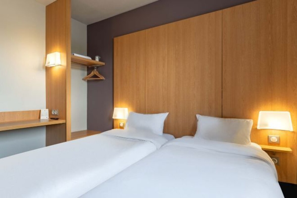 Habitació d'hotel amb un panell de capçal de fusta, dos llits, abacines, una prestatgeria de fusta i una perxa per a abrics.