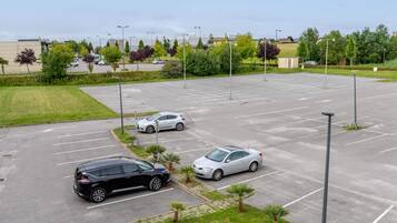 Ein Parkplatz mit mehreren Autos, umgeben von Grünflächen und Gebäuden im Hintergrund.