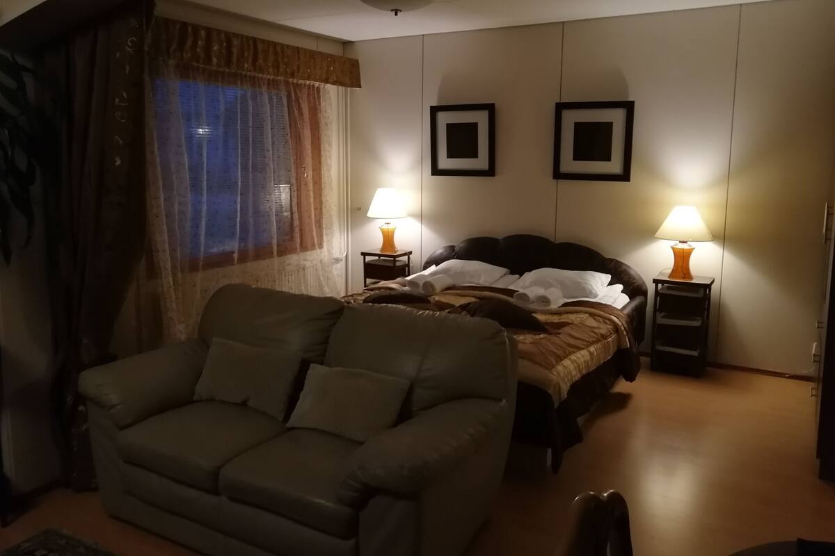 A hotel room with a bed, two bedside lamps, a sofa, and a window with curtains.