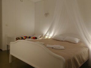 Una cama con estructura blanca, colcha color beige y dosel blanco.