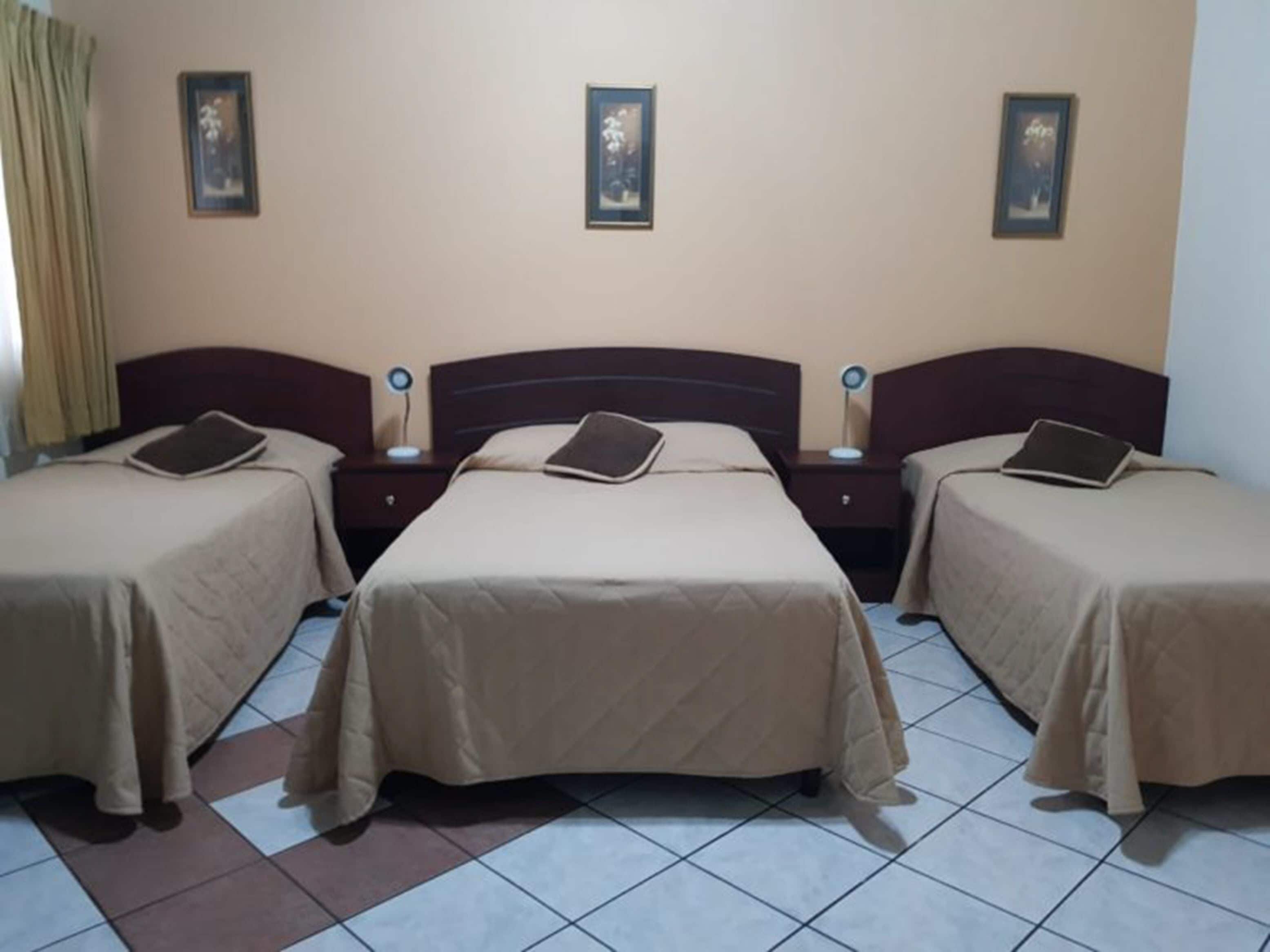 Una habitación de hotel con tres camas individuales, cada una con cabecero, mesitas de noche y lámparas.