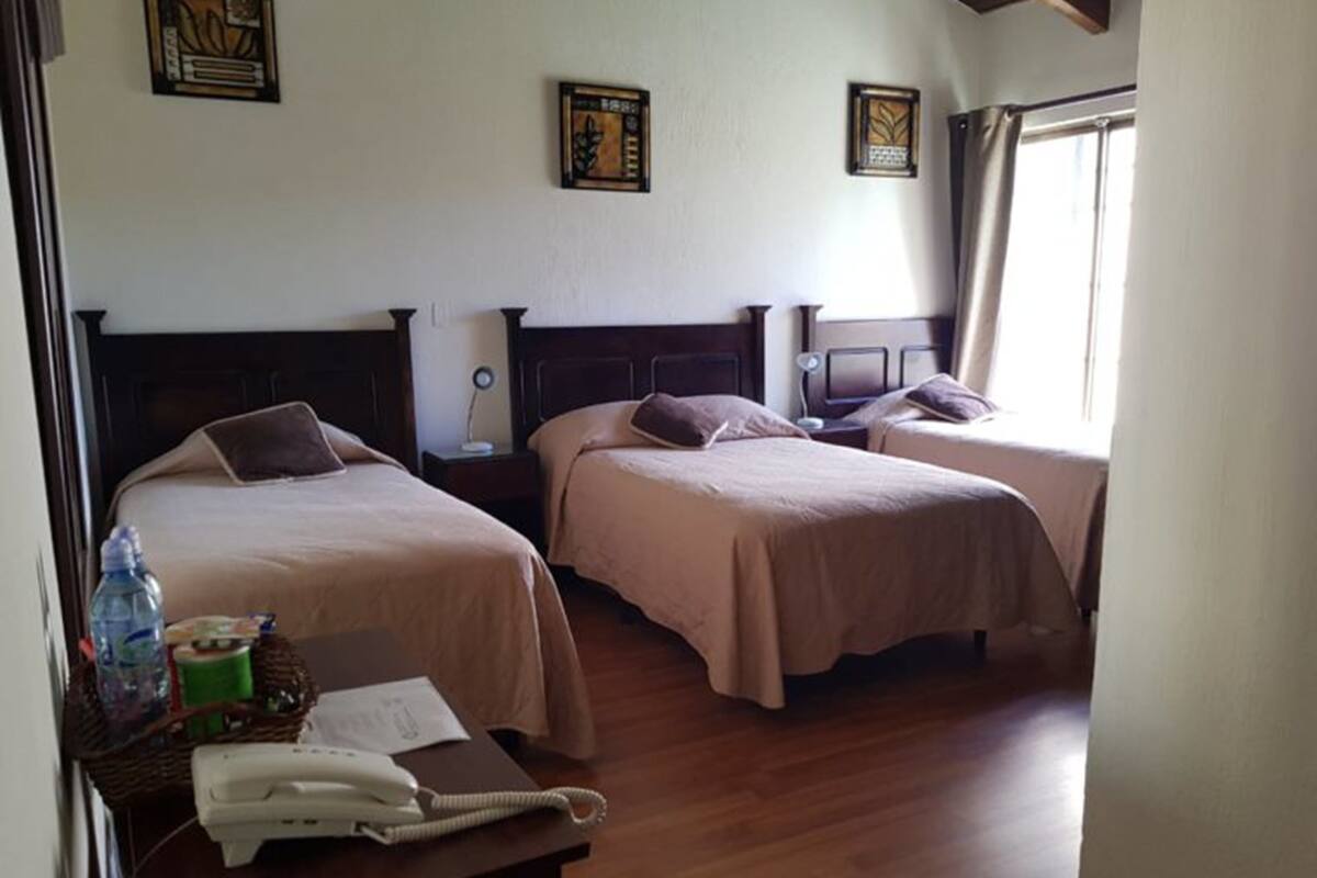 Una habitación de hotel con tres camas, suelo de madera y obras de arte en las paredes.