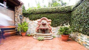 A courtyard with a decorative fountain, potted plants, and a tiled wall.