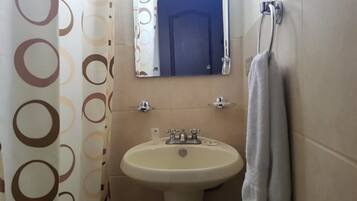 A bathroom with a sink, mirror, towel rack, and patterned shower curtain.