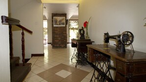 A spacious room with a tiled floor, a wooden staircase, a sewing machine, and a vase with flowers.