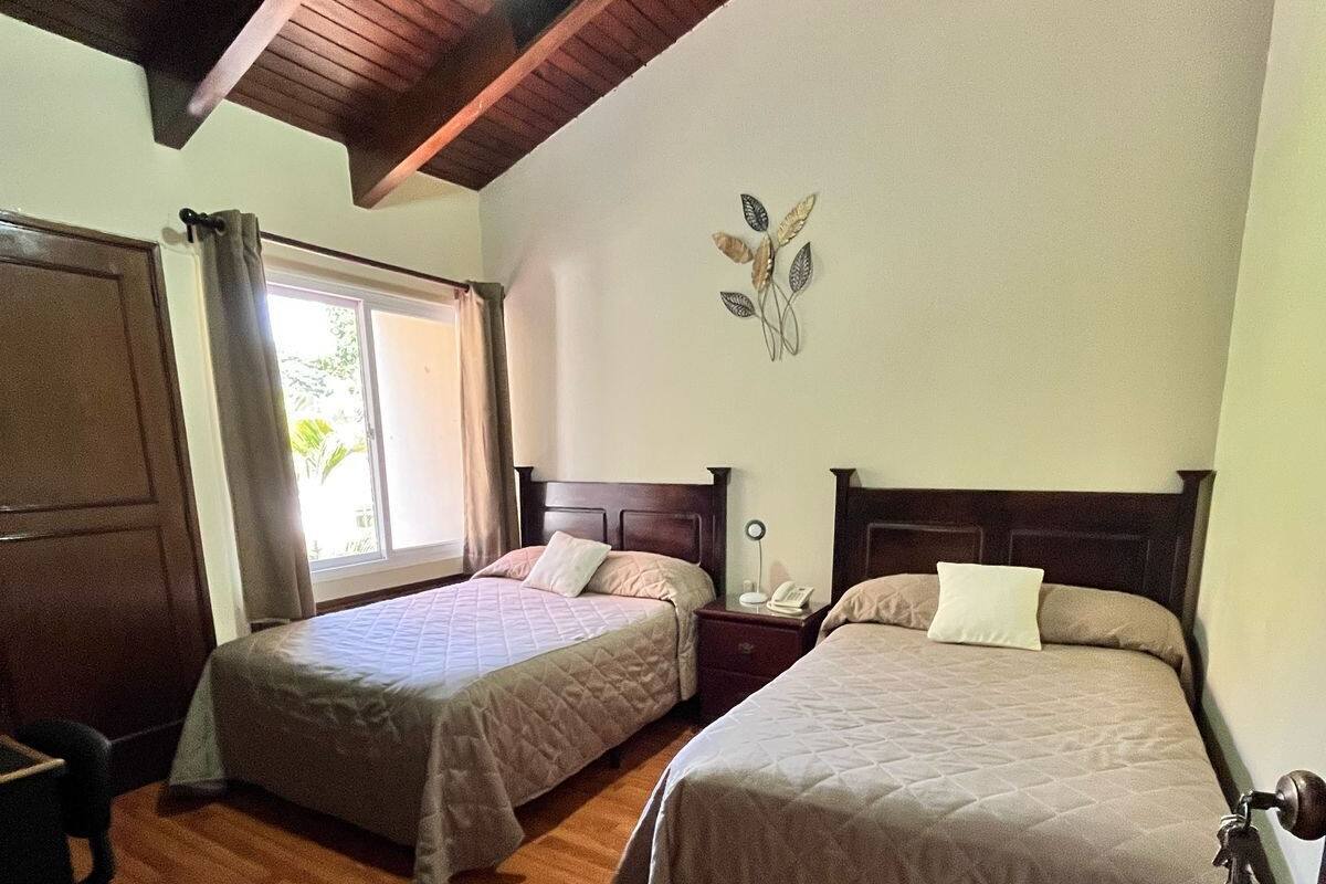Un dormitorio con dos camas, suelo de madera, ventilador de techo y una ventana con cortinas.