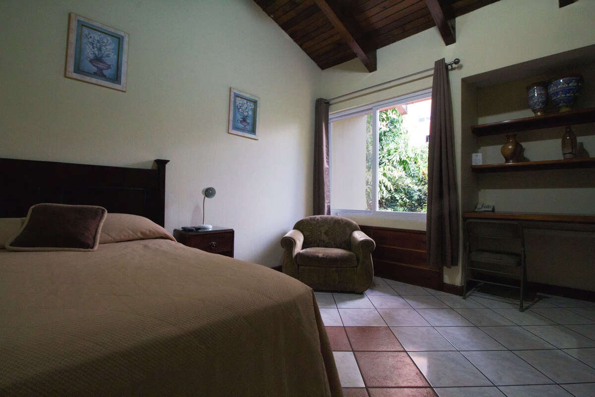 Een slaapkamer met een bed, een stoel, een bureau met planken en een raam met gordijnen.