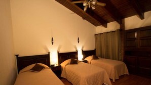 A hotel room with three single beds, wooden headboards, and bedside lamps.