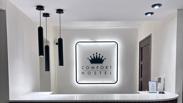 A reception desk with a sign reading "COMFORT HOSTEL" and three pendant lights above it.