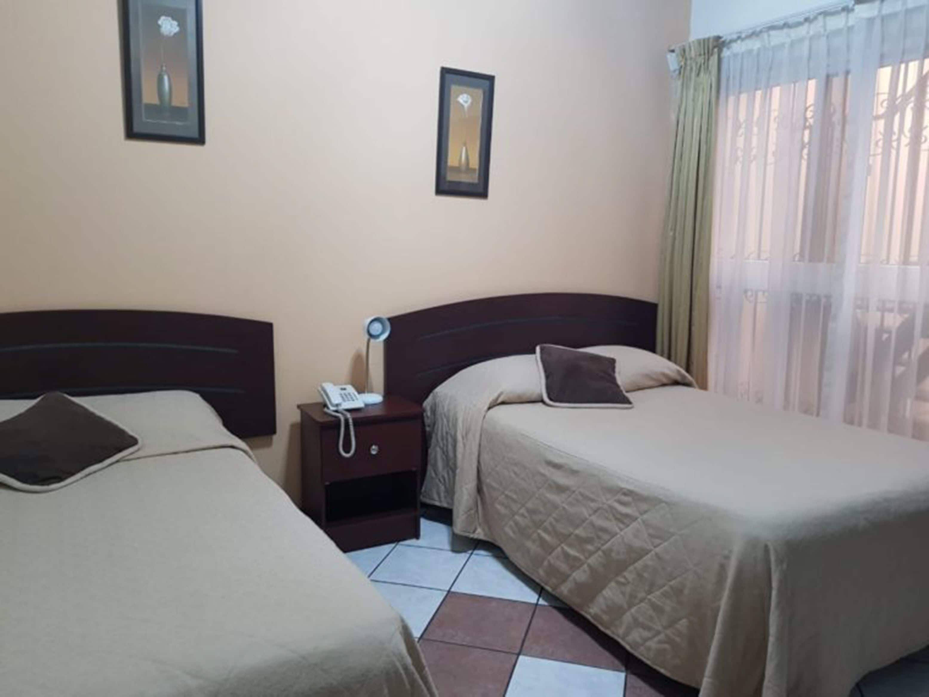 Habitación de hotel con dos camas, una mesita de noche con lámpara, teléfono y un cuadro en la pared.