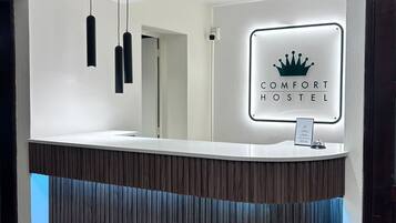 Un comptoir d’accueil au design moderne, une enseigne indiquant « COMFORT HOSTEL » et des luminaires suspendus.