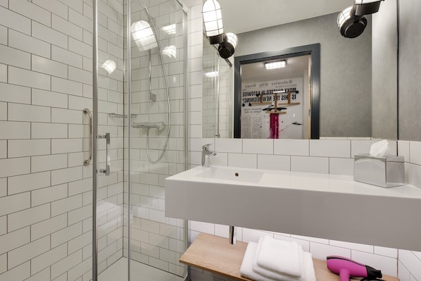 Un baño moderno con cabina de ducha de vidrio, un lavamanos blanco y un estante de madera con toallas.