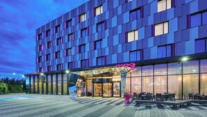 Un hotel moderno con fachada de vidrio, zona de estar al aire libre y un letrero de neón.