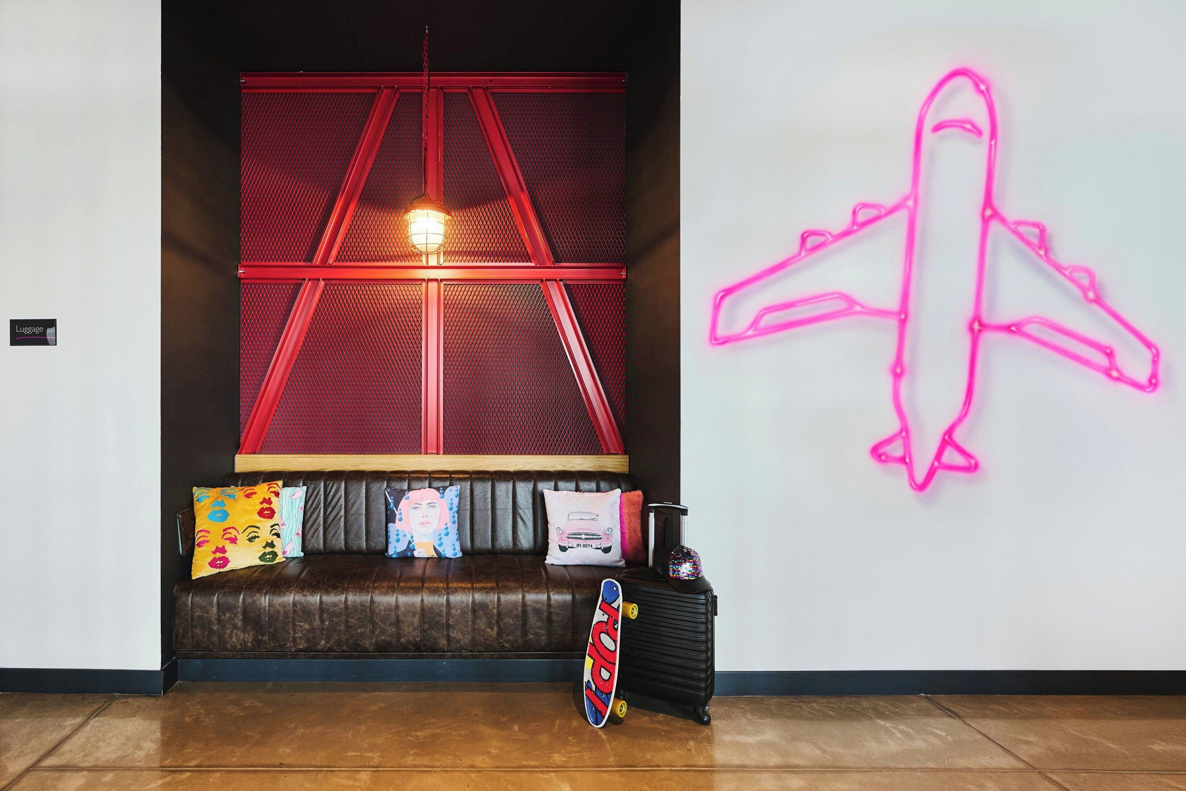 A room with a brown leather sofa, a neon airplane sign, and a skateboard.