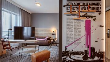 Una habitación de hotel moderna con una gran televisión de pantalla plana, un sofá, un escritorio y una mesita de café.