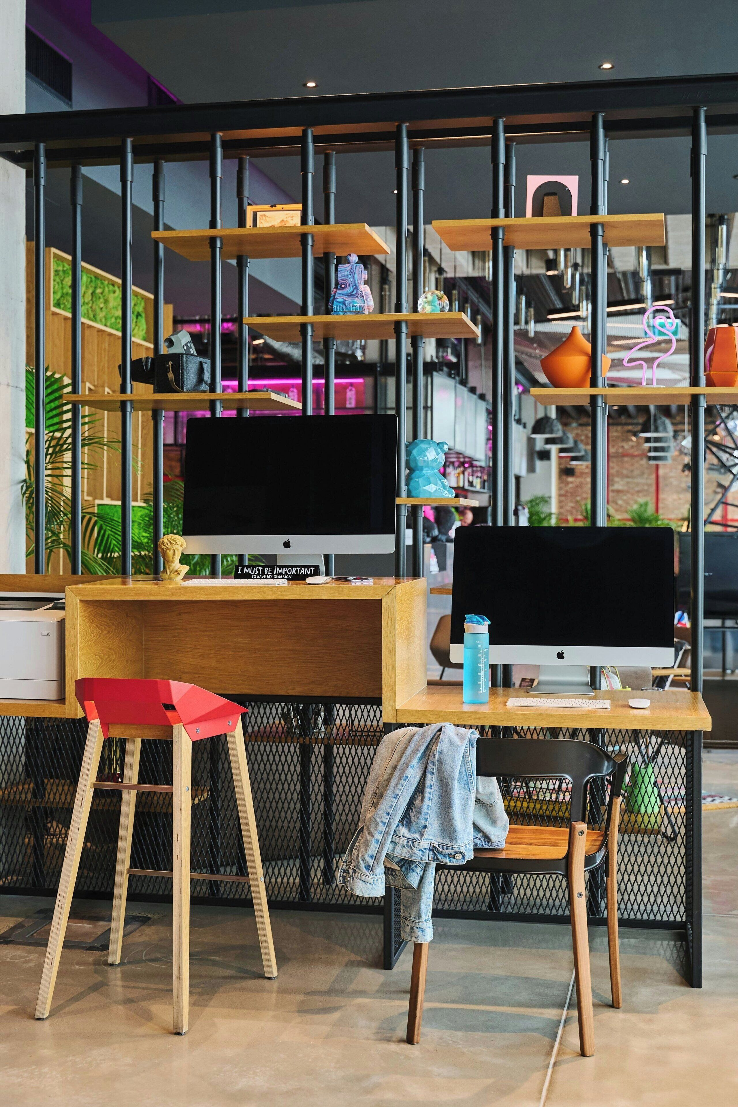 A modern workspace with two Apple iMac computers, a red stool, and a wooden desk.