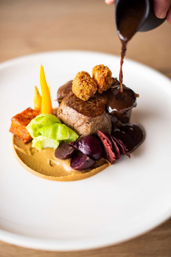 A plated dish with a variety of food items including a piece of meat, vegetables, and a sauce being poured over it.