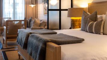 A hotel room with a large bed, a wooden headboard, a sitting area with a chair and a small table, and a window with curtains.