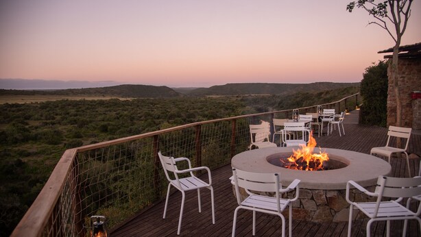 Um terraço com lareira, cadeiras brancas e vista para a paisagem.