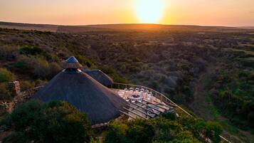 Uma construção com telhado de colmo, área de estar circular e parede de pedra.