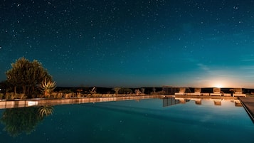 A nighttime pool area with a clear view of the sky and stars, surrounded by trees and a row of chairs.