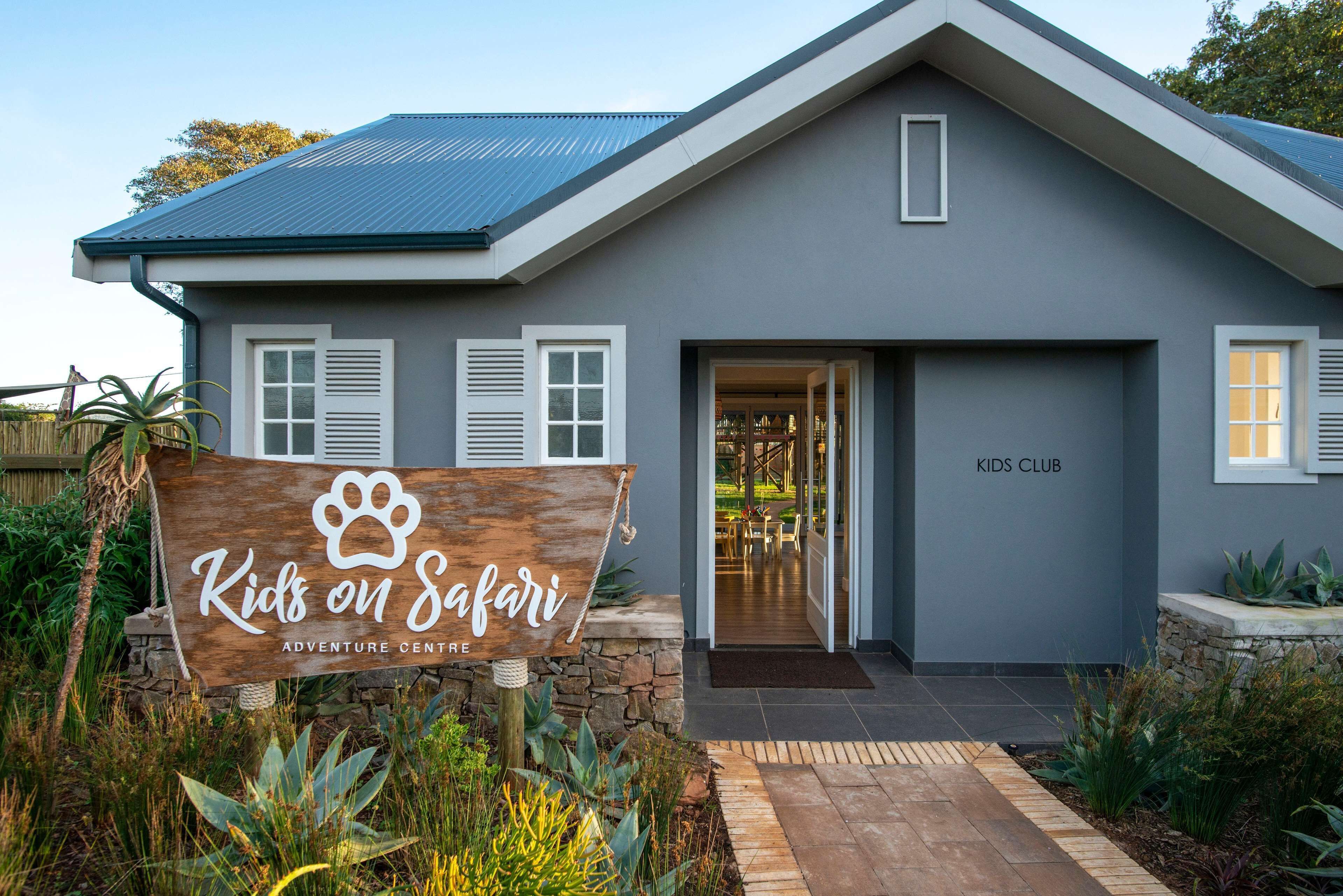 A modern building with a sign reading "Kids on Safari Adventure Center" and a "Kids Club" sign on the door.