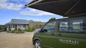 Uma carrinha verde com a inscrição "SHAMWARI PRIVATE GAME RESERVE" estacionada em frente a uma casa com varanda e cerca de madeira.