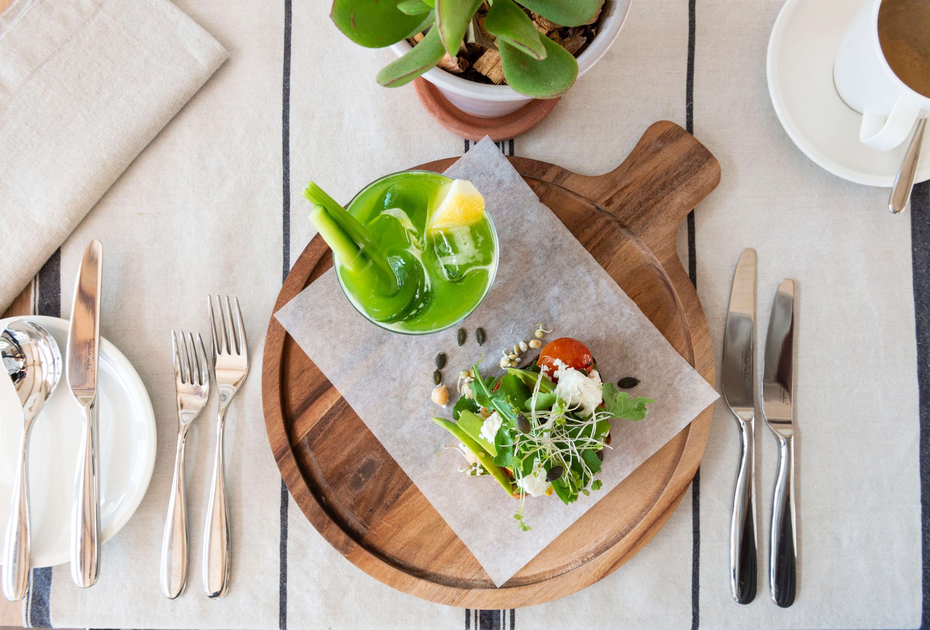 A neatly arranged table with a wooden board, a glass of green drink, and a salad on parchment paper.
