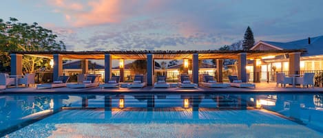 A pool area with lounge chairs and a covered seating area at dusk.