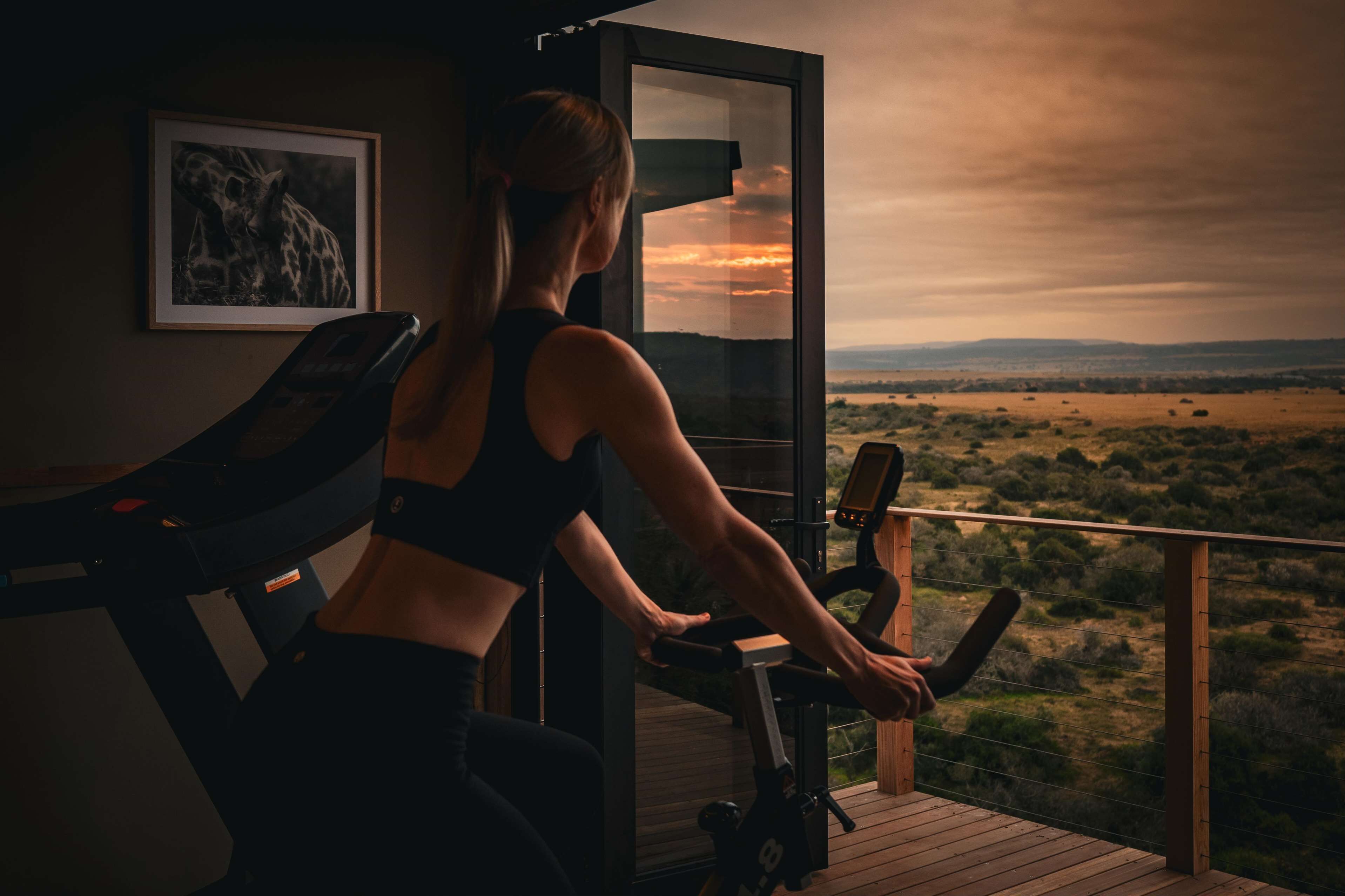 A woman exercising on a stationary bike with a scenic view of a landscape through a large window.